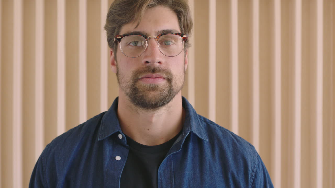 ritratto a rallentatore di un attraente giovane hipster con gli occhiali che guarda la telecamera pensoso bello serio maschio caucasico