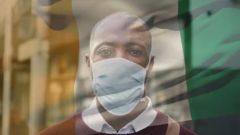 Animation of flag of cameroon waving over latin man wearing face mask in city street