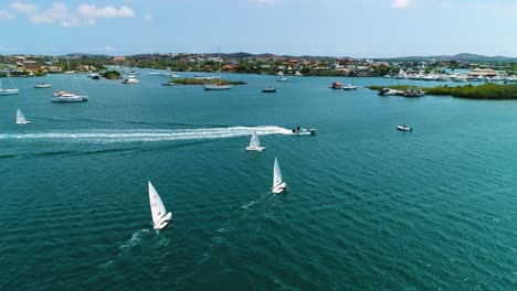 spanish waters sunfish sailboats cross across open bay of curacao, aerial descend overview