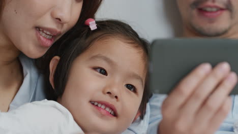Feliz-Familia-Asiática-Teniendo-Video-Chat-Usando-Un-Teléfono-Inteligente-En-La-Cama,-Madre-Y-Padre-Con-Niños-Saludando,-Charlando-Con-Amigos-Por-Teléfono-Móvil,-Disfrutando-De-La-Comunicación-En-Línea,-Imágenes-De-4k