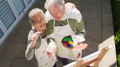 happy diverse senior couple painting in garden on sunny day