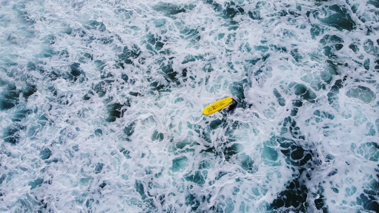 A surfer in a black wetsuit swimming with a yellow surfboard in the sea, waiting for the right wave - aerial static shot