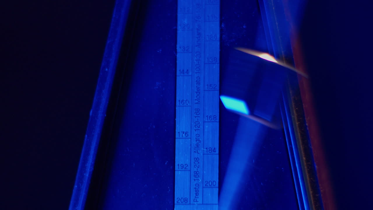 Primer plano del péndulo de un metrónomo oscilando con luz azul