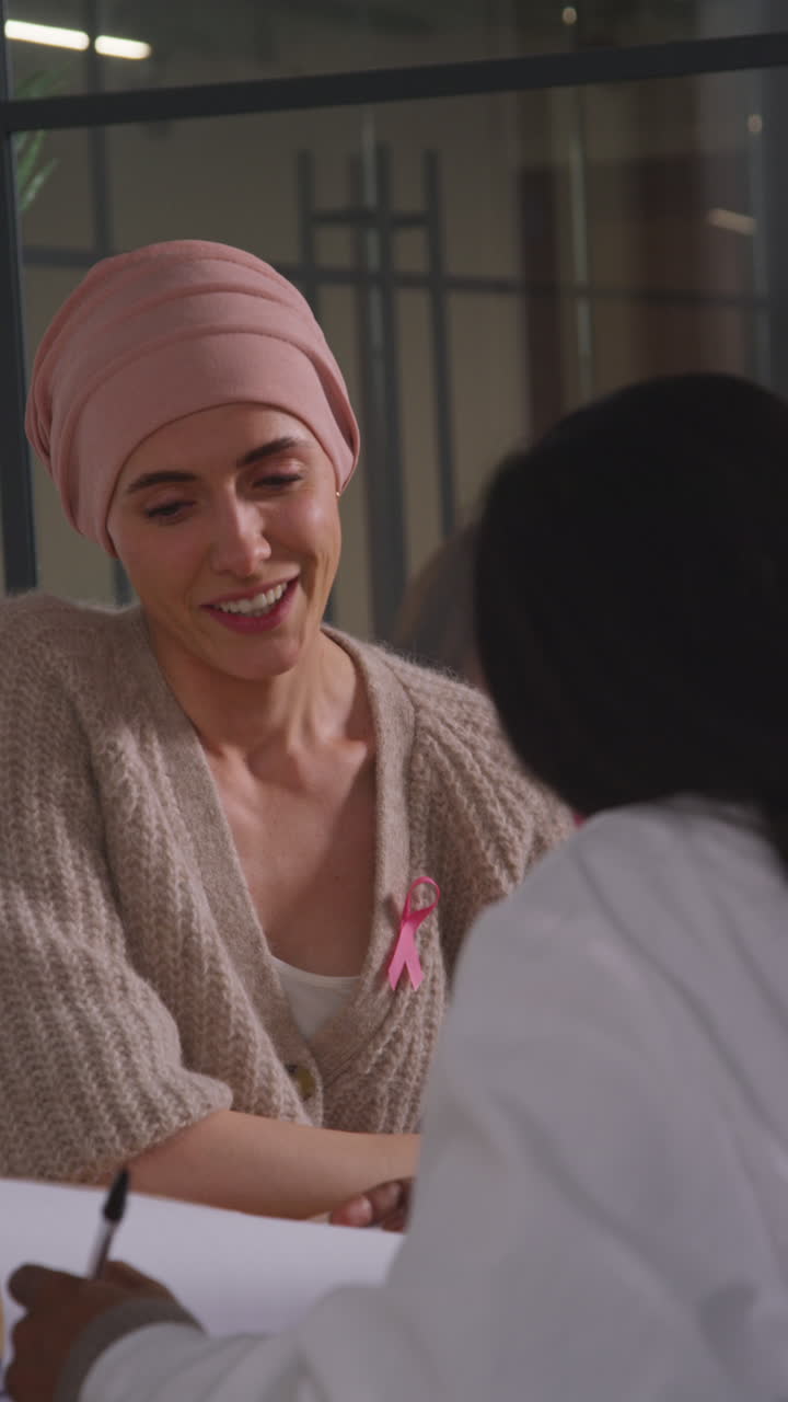 Vertical Video Of Young Woman Patient Wearing Headscarf Undergoing Chemotherapy Treatment For Breast Cancer Meeting With Oncologist Or Doctor In Hospital 1