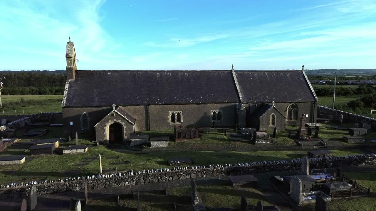 St Peters church in rural Newborough aerial view flight across Welsh slate gravestones at sunrise