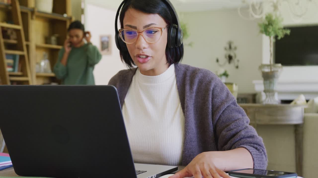 una adolescente biracial feliz sentada en la mesa y usando una computadora portátil, en cámara lenta