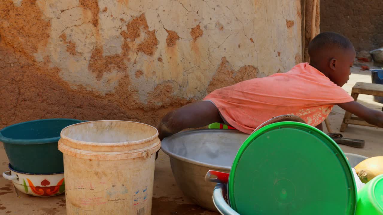 young child children black kid of Africa washing dishes in remote rural village close up