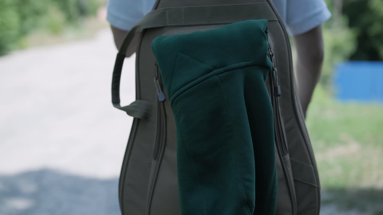 молодой человек идет с гитарой по улице возле леса