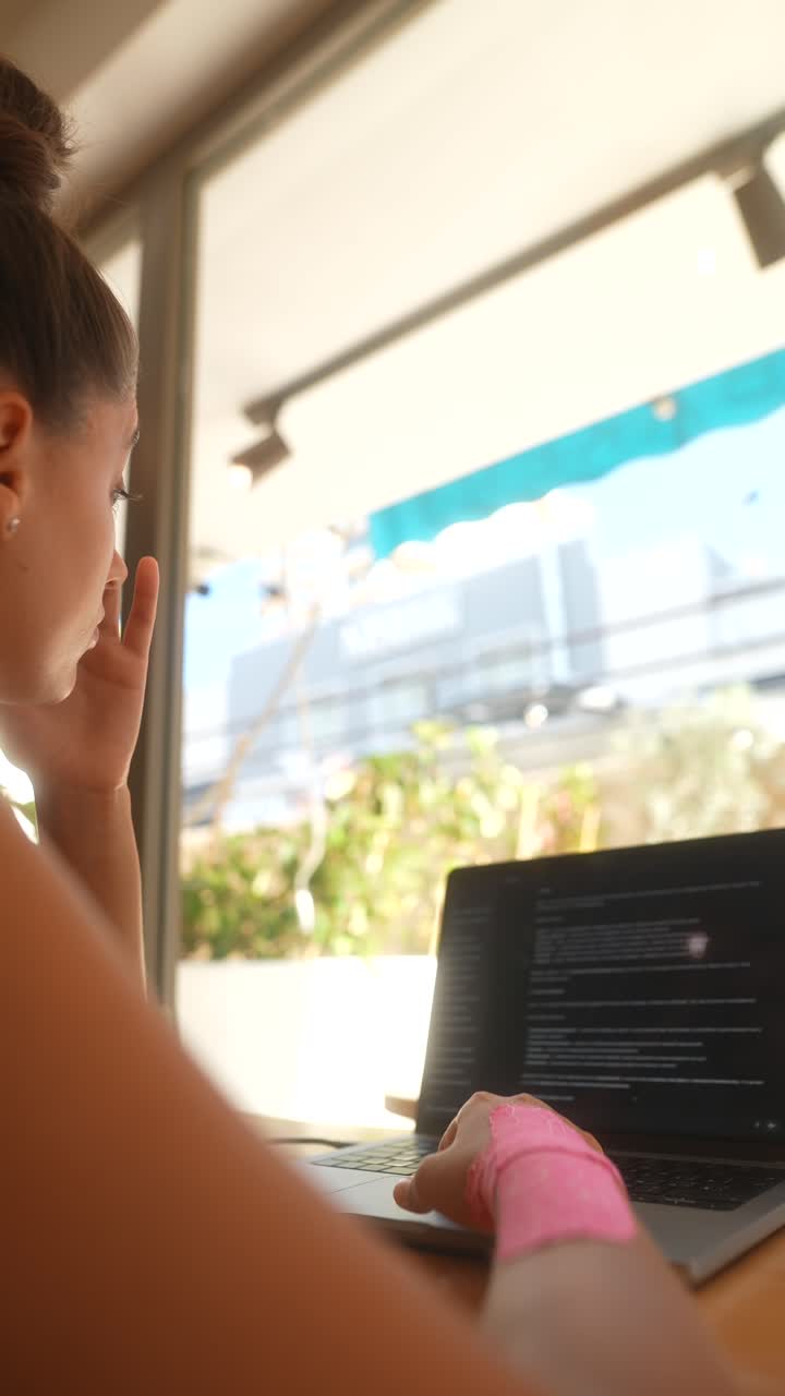 mujer trabajando en una computadora portátil en un café con una muñeca lesionada