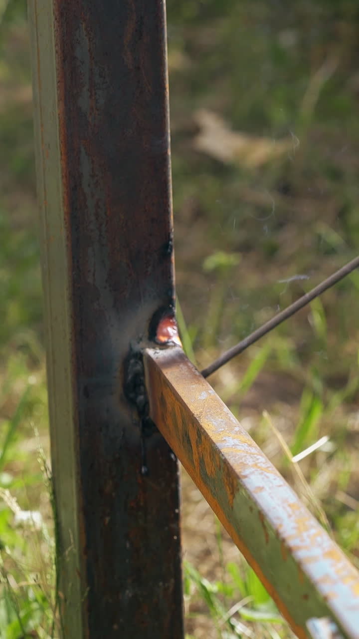 close view builder in protective gloves welds rail to fence pole with sparks and smoke at country house