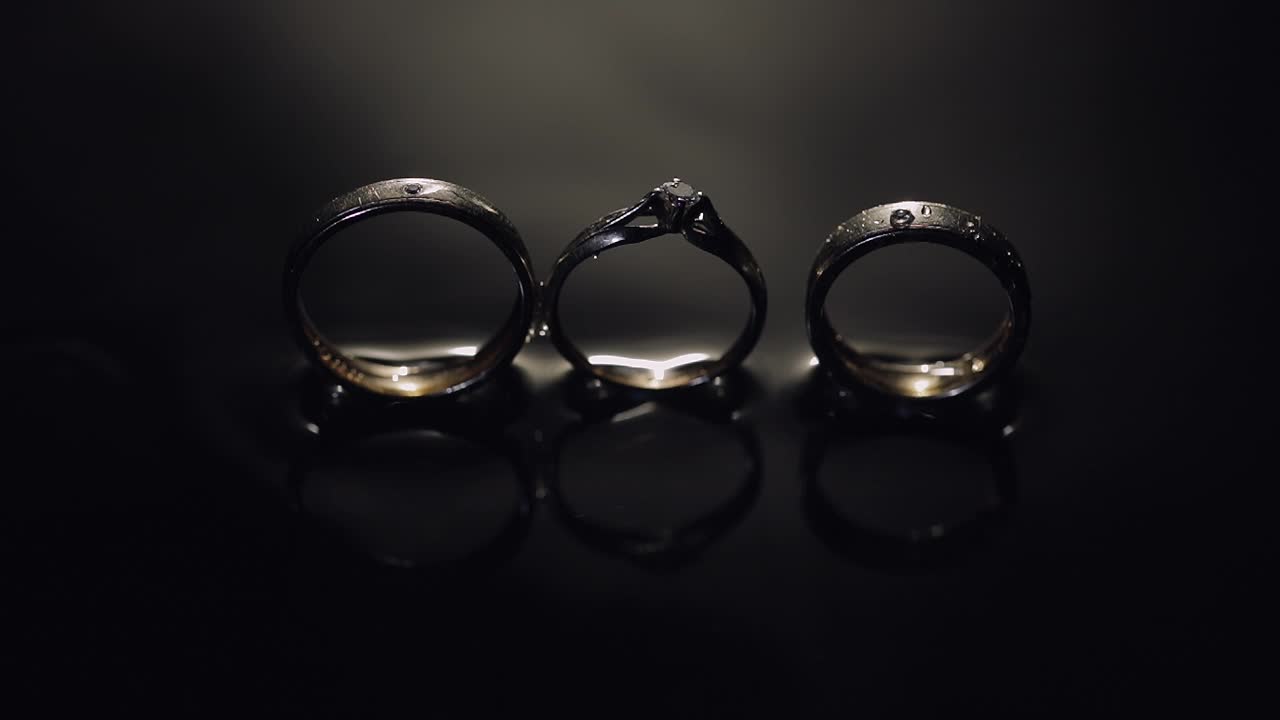 Wedding and engagement rings lying on dark water surface shining with light