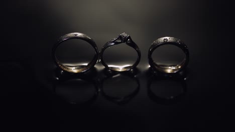 wedding and engagement rings lying on dark water surface shining with light