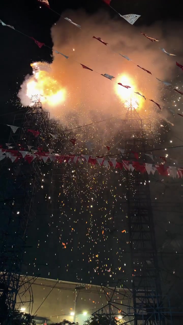 Tall fireworks towers erupt with sparks and smoke at night during a festive celebration