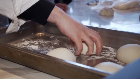 Chef-puts-divided-pizza-dough-pieces-into-metal-storage-tray