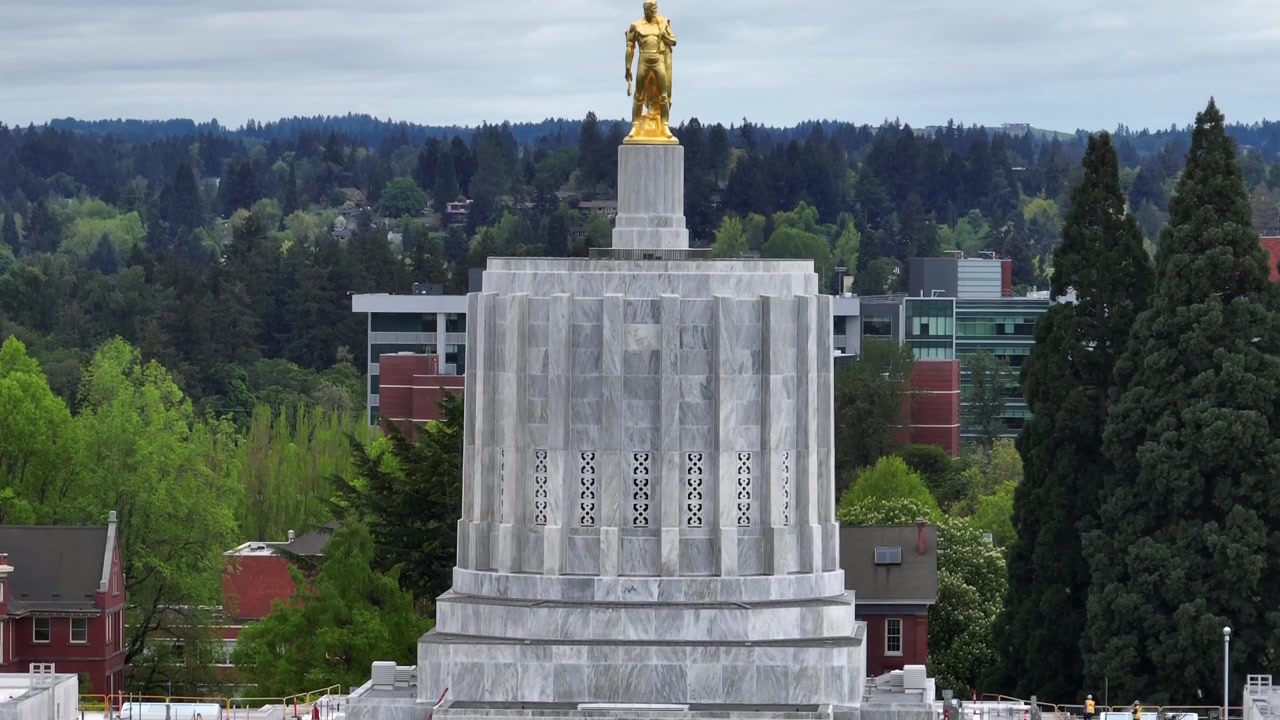 Edificio del Campidoglio dello Stato dell'Oregon a Salem con la statua dorata dell'Oregon Pioneer su una torre di marmo bianco circondata da alberi verdi lussureggianti in una giornata nuvolosa negli Stati Uniti. Ripresa aerea ascendente