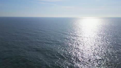 Viaje-Aéreo-Sobre-La-Extensión-Serena-Del-Océano-En-Calma,-Mientras-Los-Rayos-Dorados-Del-Sol-Bajo-Iluminan-Las-Suaves-Olas