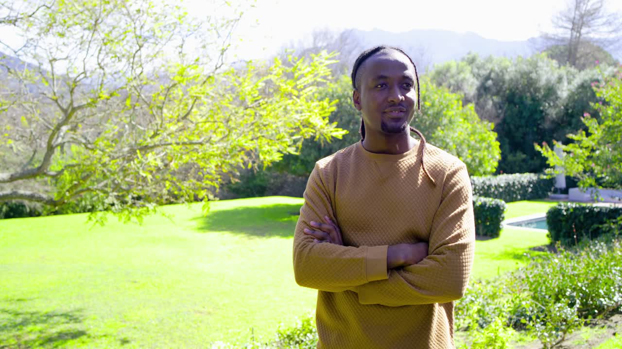 African American man arms crossed yard seeing camera zooming in turning head, smiling, copy space