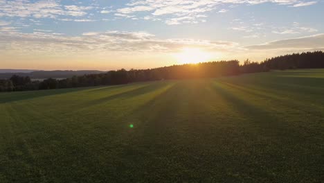 Vista-De-Drones-Mientras-Vuela-Sobre-Un-Prado-Alejándose-De-La-Puesta-De-Sol