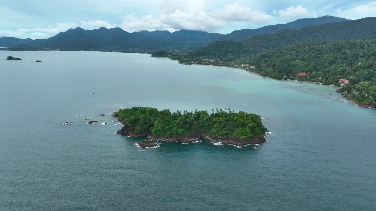 Small tropical island surrounded by turquoise water off Lonely Beach, Koh Chang, Trat, Thailand, showing lush jungle coastline and calm sea under cloudy skies, aerial view