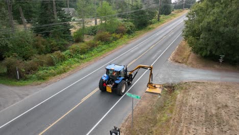 田舎道の土手で生い茂った雑草を刈るトラクターに続いて撮影されたドローン