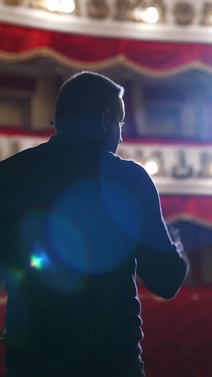 Speaker on stage against bright spotlight. Back view of an actor man during the rehearsal in the classical theater. Vertical video