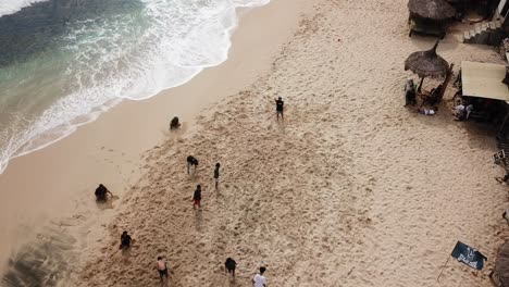 aerial-view,-showing-tourists-playing-beach-soccer-on-Watu-Lawang-beach,-Gunung-Kidul,-Yogyakarta,-Indonesia