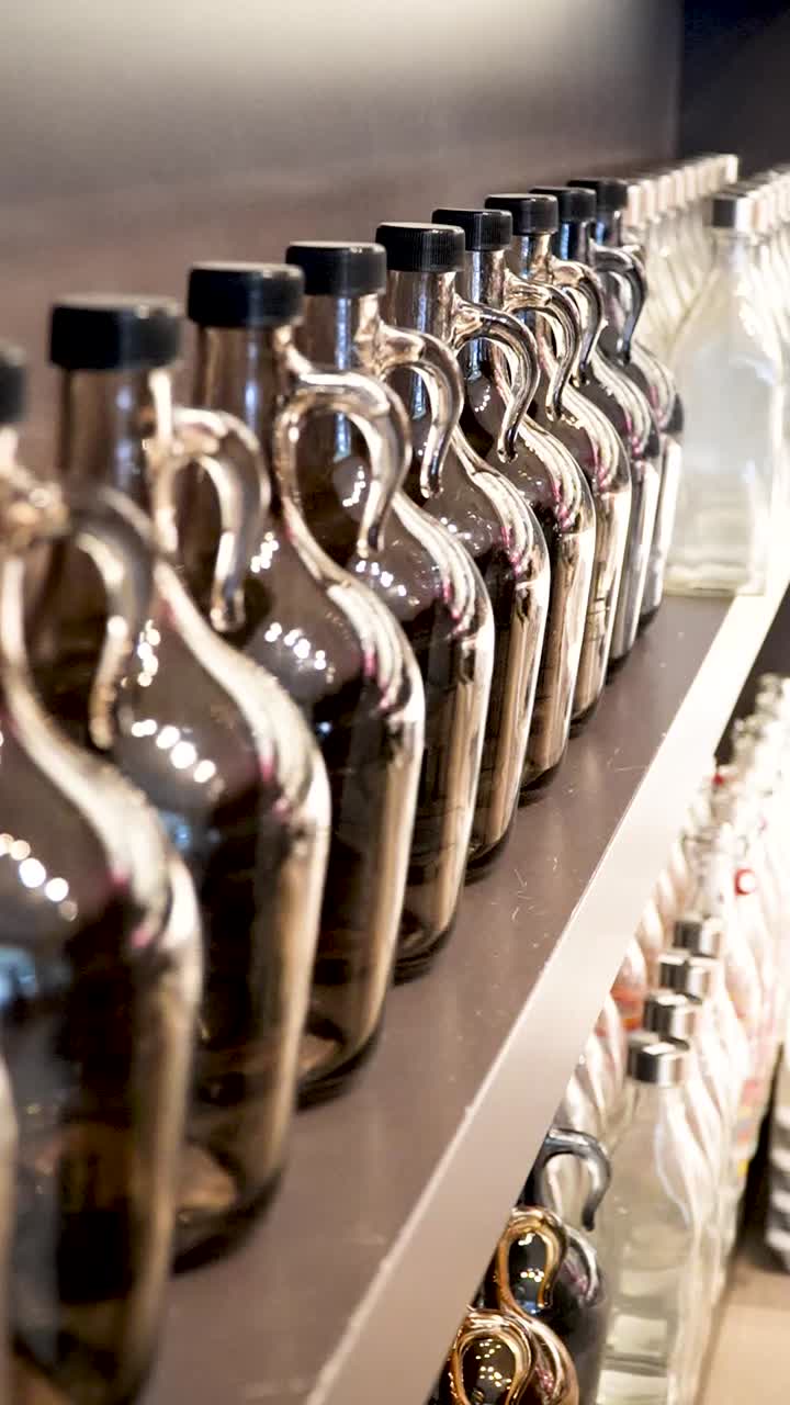 Rows of glass bottles sit neatly on a shelf, reflecting light and showcasing various drinks. The arrangement highlights the craftsmanship and variety available for customers