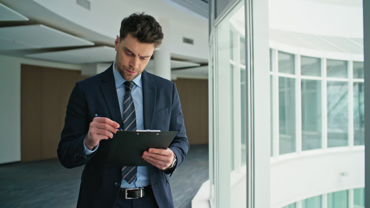 Thoughtful executive reading documents on clipboard walking corridor closeup