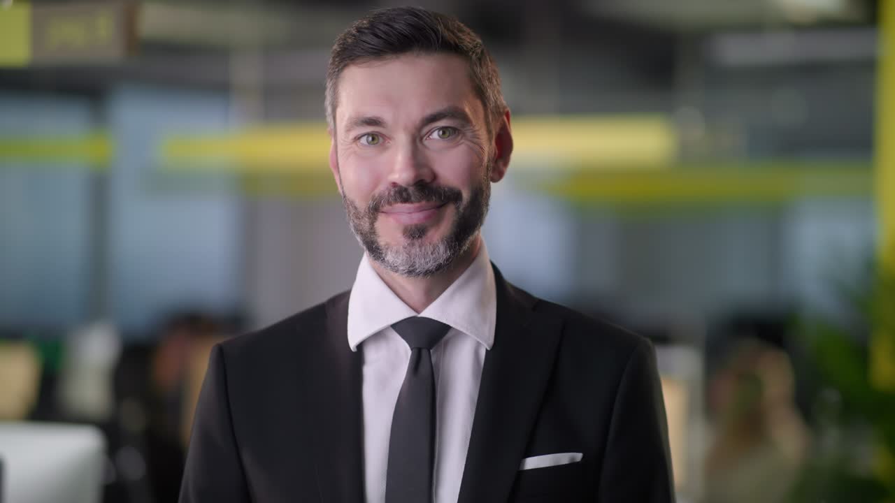 retrato de un hombre de negocios adulto jefe de pie en la oficina sonriendo mirando a la cámara mientras los empleados están ocupados trabajando en el fondo