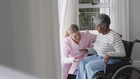 smiling caucasian nurse with senior african american woman patient in wheelchair, slow motion