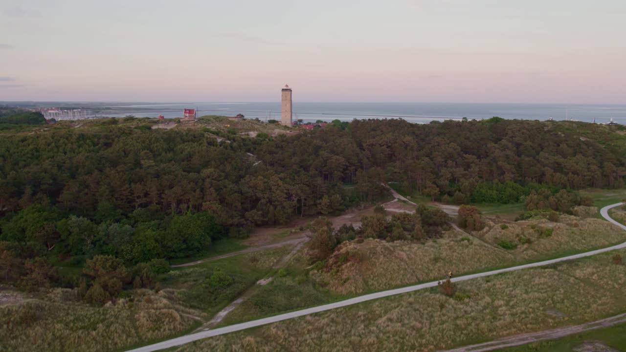 Ciclista che si gode il tramonto su un sentiero di ghiaia e il Brandaris, Terschelling, Frisia