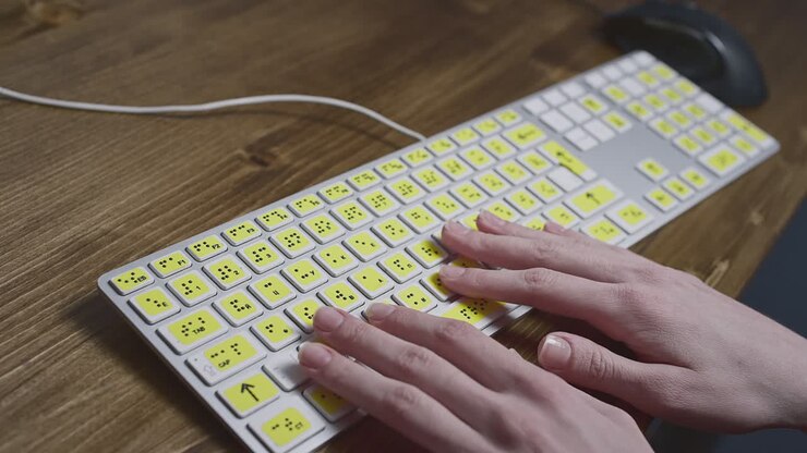 Close-up of a computer keyboard with braille. A blind girl is typing words on the buttons with her hands. Technological device for visually impaired people.