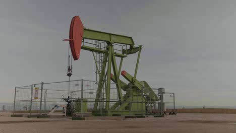 steady shot of a green-orange oil derrick moving