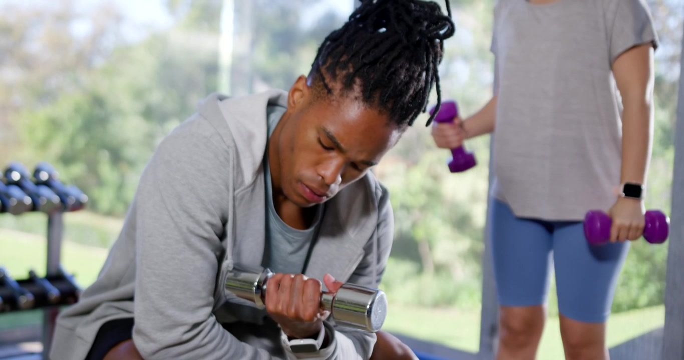 African American duo with man curling silver weight after rest while woman lifting purple weights