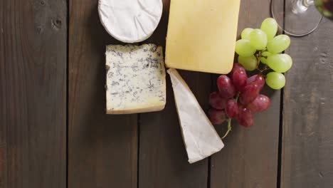 Video-of-diverse-cheeses,-grapes-and-wine-on-wooden-surface