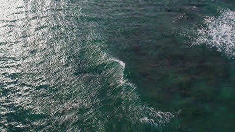 a drone swoops down to the crystal clear green water of the pacific ocean as white capped waves break before the shore on the island of oahu