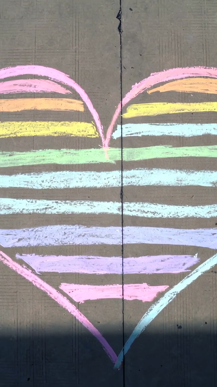 Vertical video: Shifting sunlight casting dark shadow across rainbow chalk heart on concrete