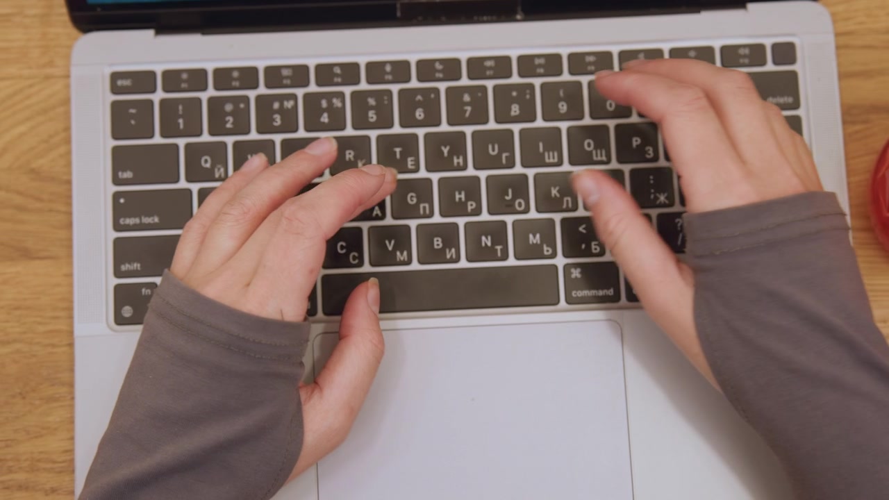 Overhead hands typing on keyboard over wooden desk in bright daylight, fingerless glove sleeves, fastpaced focused workflow with coffee mug at edge, professional composing messages and emails