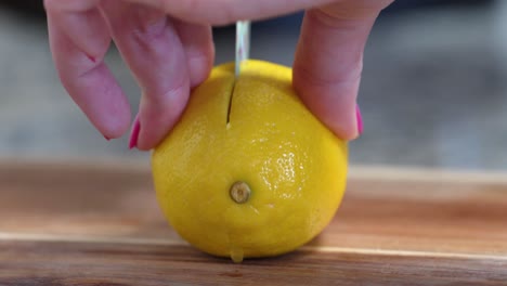 woman slicing yellow lemon in half close up on wooden cutting board with small knife decorated with flowers, hands with pink nail polish