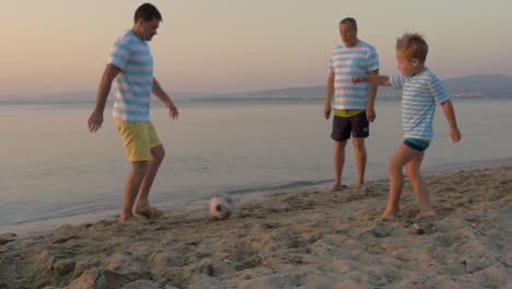 men of three generations playing football on beach