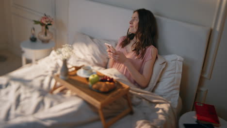 home girl enjoying time alone in bed. dreamy relaxed woman using mobile phone