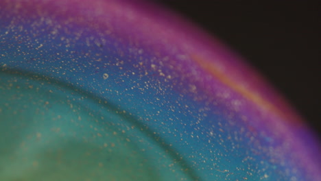 close up shot of a rainbow colored sphere - small particles moving on the surface - black studio background - shallow depth of field - static camera