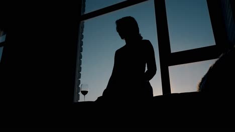 Silhouette-Eines-Mädchens,-Das-Bei-Sonnenuntergang-Neben-Einem-Weinglas-Im-Zimmer-Sitzt