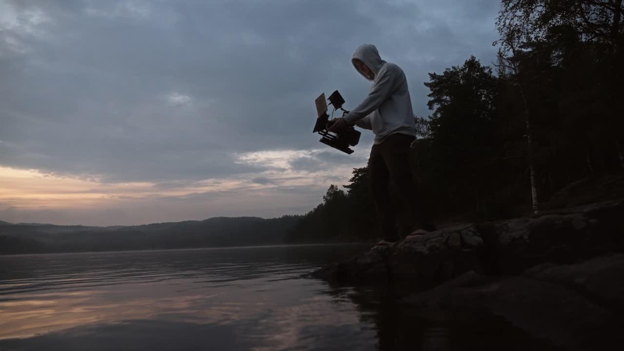 A person filming a lake landscape with a cinema camera in Norway during sunset