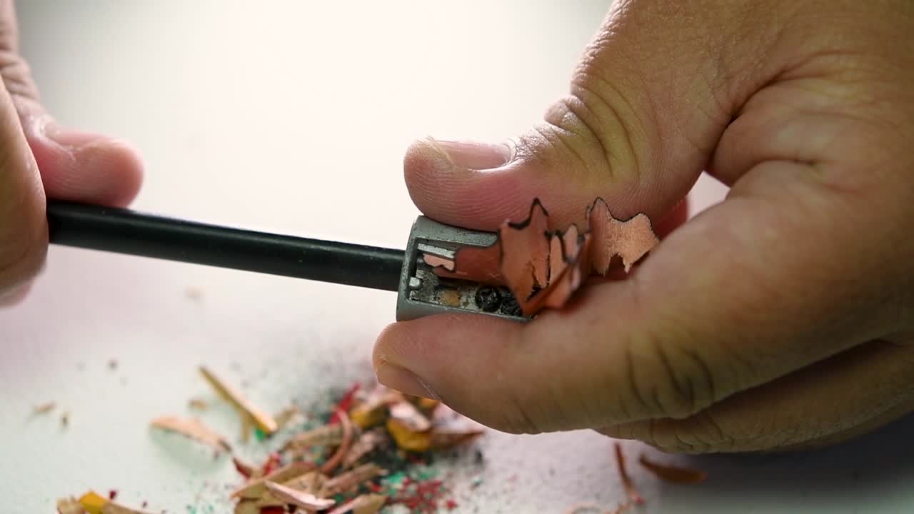 imágenes de manos afilando lentamente un lápiz y algunos lápices de colores con un sacapuntas de cuña