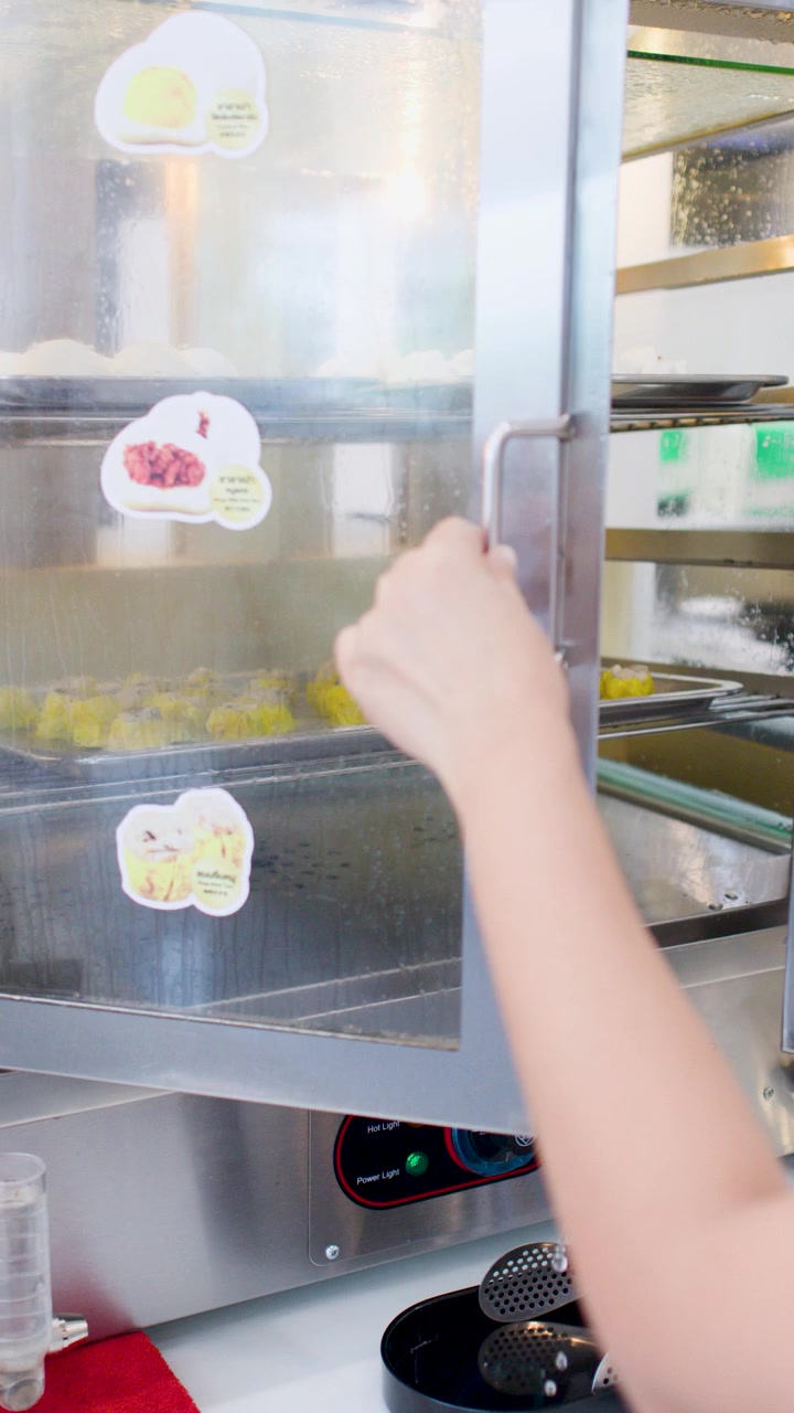 Una mano chiude la porta di vetro di una vaporiera per alimenti in acciaio inossidabile contenente ravioli asiatici.