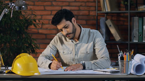 joven arquitecto árabe sentado en el escritorio de la oficina y trabajando en los nuevos dibujos del proyecto