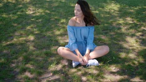 Portrait-of-attractive-brunette-woman-in-blue-dress-sitting-in-a-park