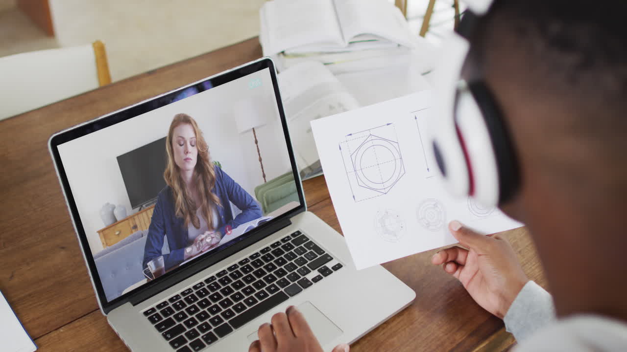estudiante universitario afroamericano que sostiene notas mientras hace una videollamada en una computadora portátil en casa