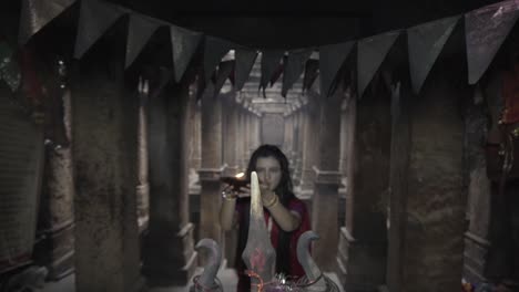 beautiful-Indian-girl-in-old-stepwell-wearing-traditional-Indian-red-saree,-gold-jewellery-and-bangles-holding-fire-plate